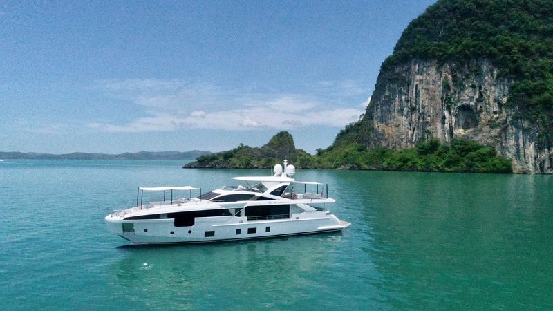 The yacht at anchor off a limestone island, three-quarter view